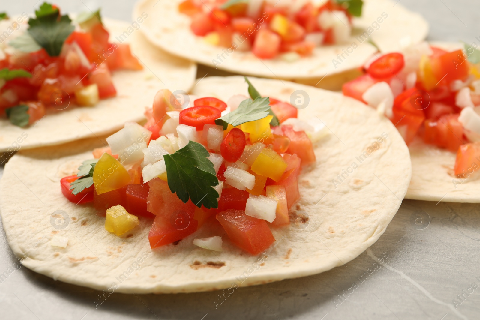 Photo of Delicious tacos with vegetables and parsley on grey table, closeup