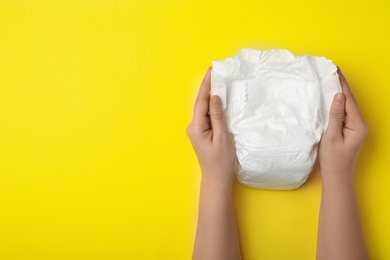 Woman with diaper on yellow background, closeup. Space for text