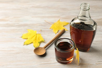 Tasty maple syrup, spoon and leaves on wooden table. Space for text