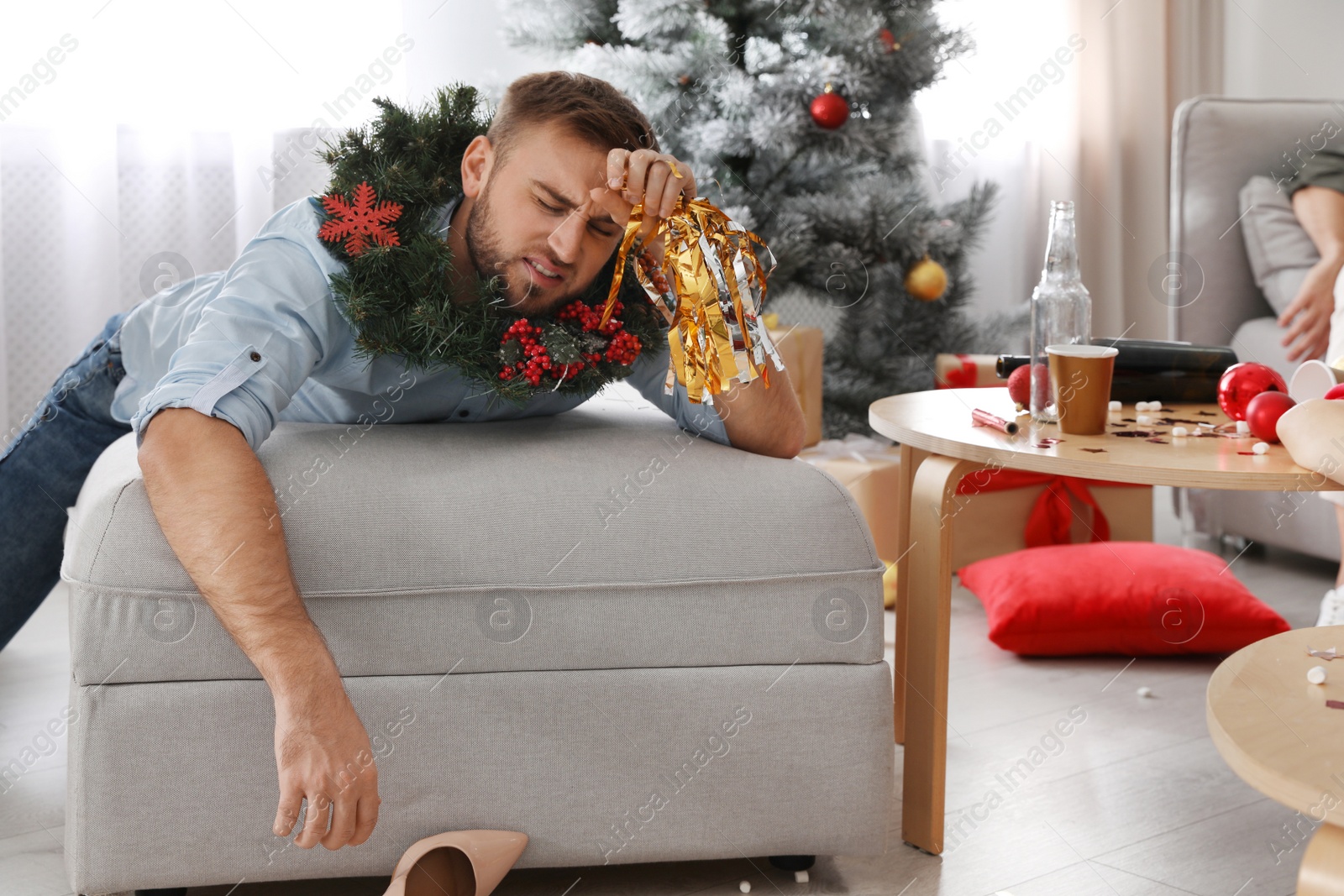 Photo of Young man suffering from hangover in messy room after New Year party