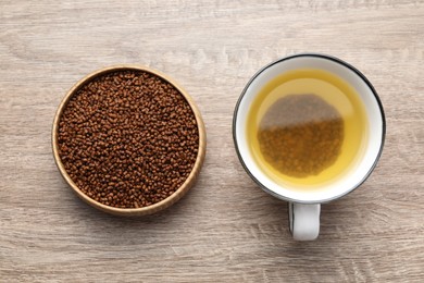 Photo of Buckwheat tea in cup and bowl with granules on wooden table, flat lay