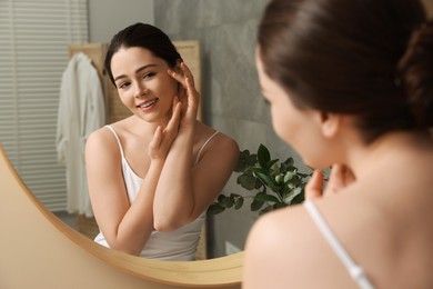 Young woman massaging her face near mirror in bathroom