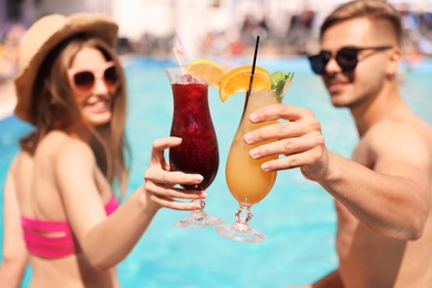 Young couple with cocktails near pool on sunny day, closeup