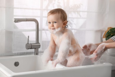 Mother washing her little baby in sink at home