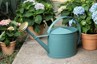 Photo of Watering can and beautiful blooming hortensia plants in pots outdoors