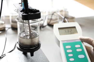 Photo of Scientist measuring acidity and pH of soil at table, closeup. Laboratory analysis