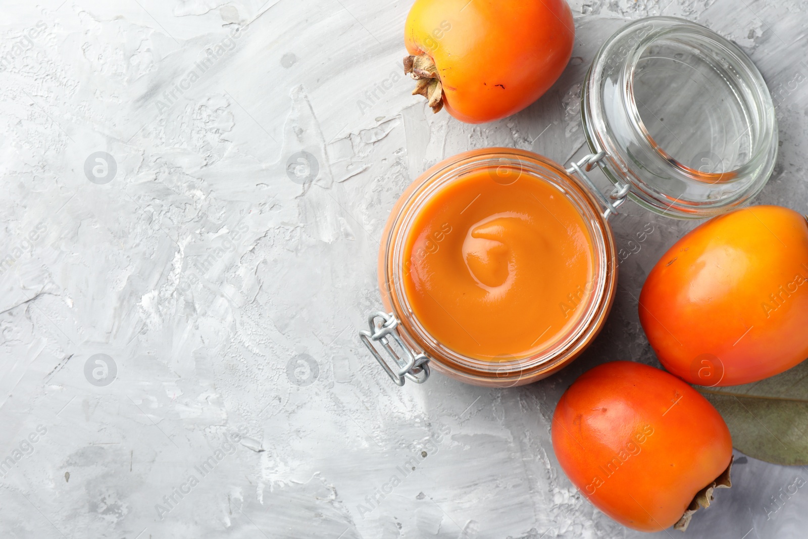 Photo of Delicious persimmon jam and fresh fruits on grey table, flat lay. Space for text