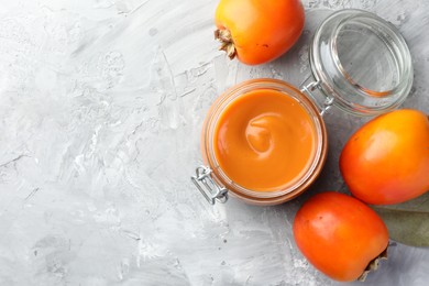 Delicious persimmon jam and fresh fruits on grey table, flat lay. Space for text