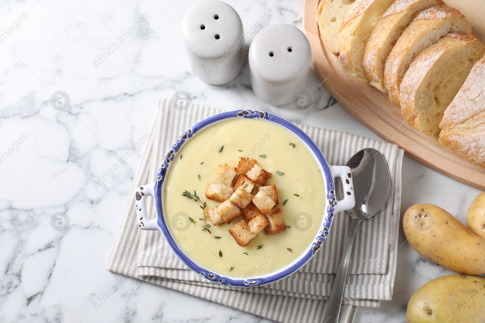 Photo of Tasty potato soup with croutons and rosemary in ceramic pot served on white marble table, flat lay