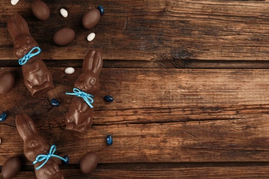 Chocolate Easter bunnies, candies and eggs on wooden table, flat lay. Space for text