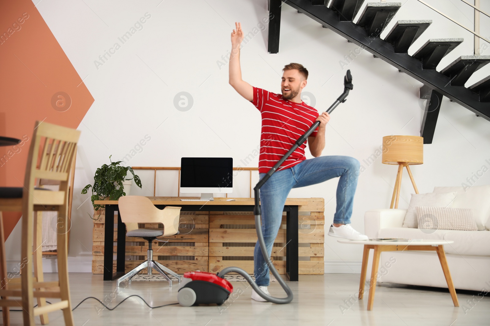 Photo of Young man having fun while vacuuming at home