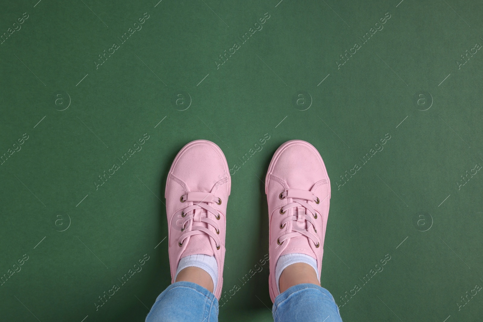 Photo of Woman in stylish sneakers standing on green background, top view