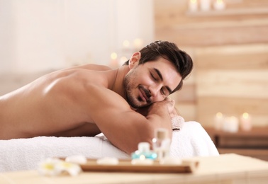 Handsome young man relaxing on massage table in spa salon, space for text