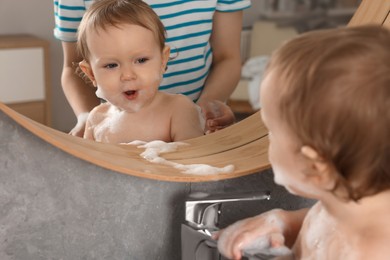 Mother washing her little baby in sink at home, closeup