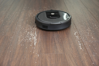 Photo of Modern robotic vacuum cleaner removing scattered rice from wooden floor