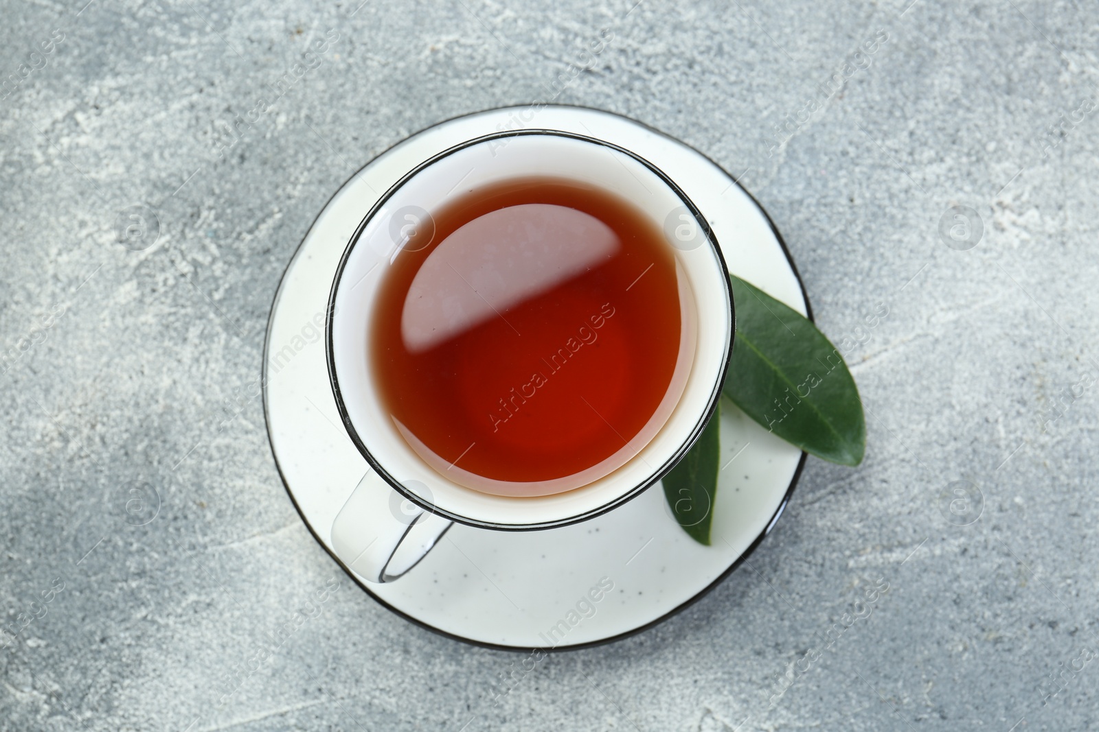 Photo of Aromatic tea in cup and green leaves on grey table, top view