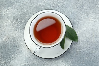 Aromatic tea in cup and green leaves on grey table, top view