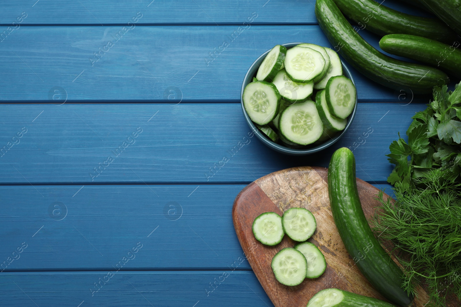 Photo of Fresh ripe cucumbers and greens on blue wooden table, flat lay. Space for text