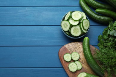 Fresh ripe cucumbers and greens on blue wooden table, flat lay. Space for text