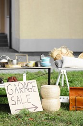 Sign Garage sale written on cardboard near tables with different stuff in yard