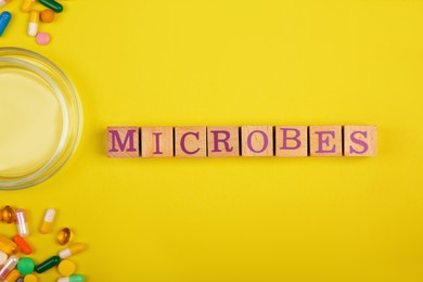 Photo of Word Microbes made with wooden cubes, pills and magnifying glass on yellow background, top view