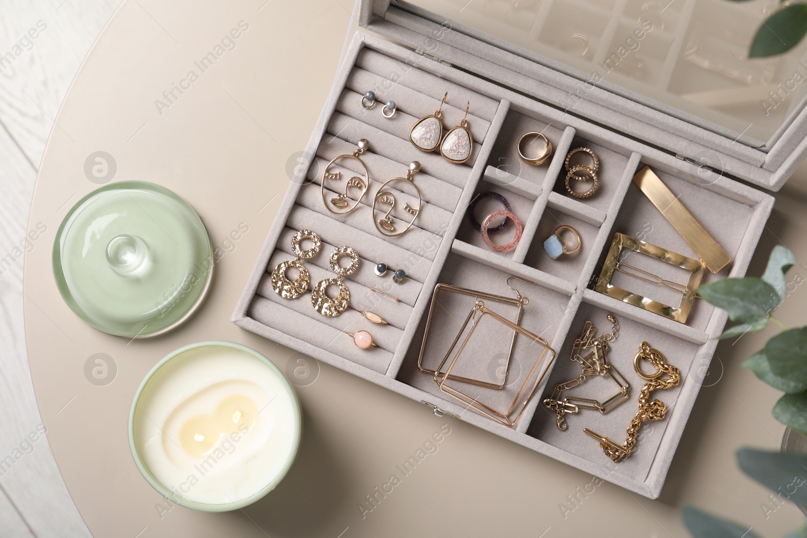 Photo of Elegant jewelry box with beautiful bijouterie and candle on beige table, flat lay