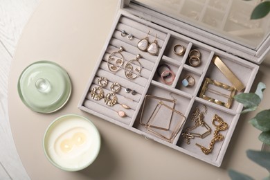 Elegant jewelry box with beautiful bijouterie and candle on beige table, flat lay