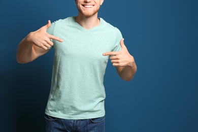 Photo of Young man wearing blank t-shirt on blue background, closeup. Mockup for design