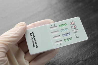 Photo of Doctor holding multi-drug screen test at black textured table, closeup