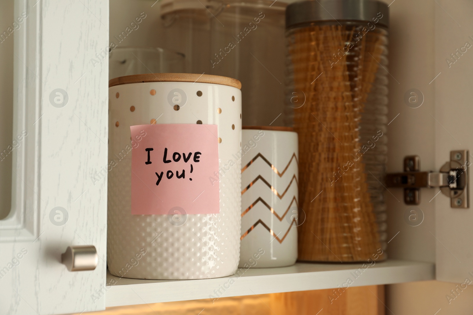 Photo of Sticky paper with words I Love You on jar in kitchen cabinet