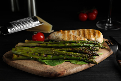 Photo of Tasty grilled chicken fillet served with asparagus on wooden board