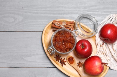 Photo of Delicious apple jam in jar, fresh fruits and spices on grey wooden table, flat lay. Space for text