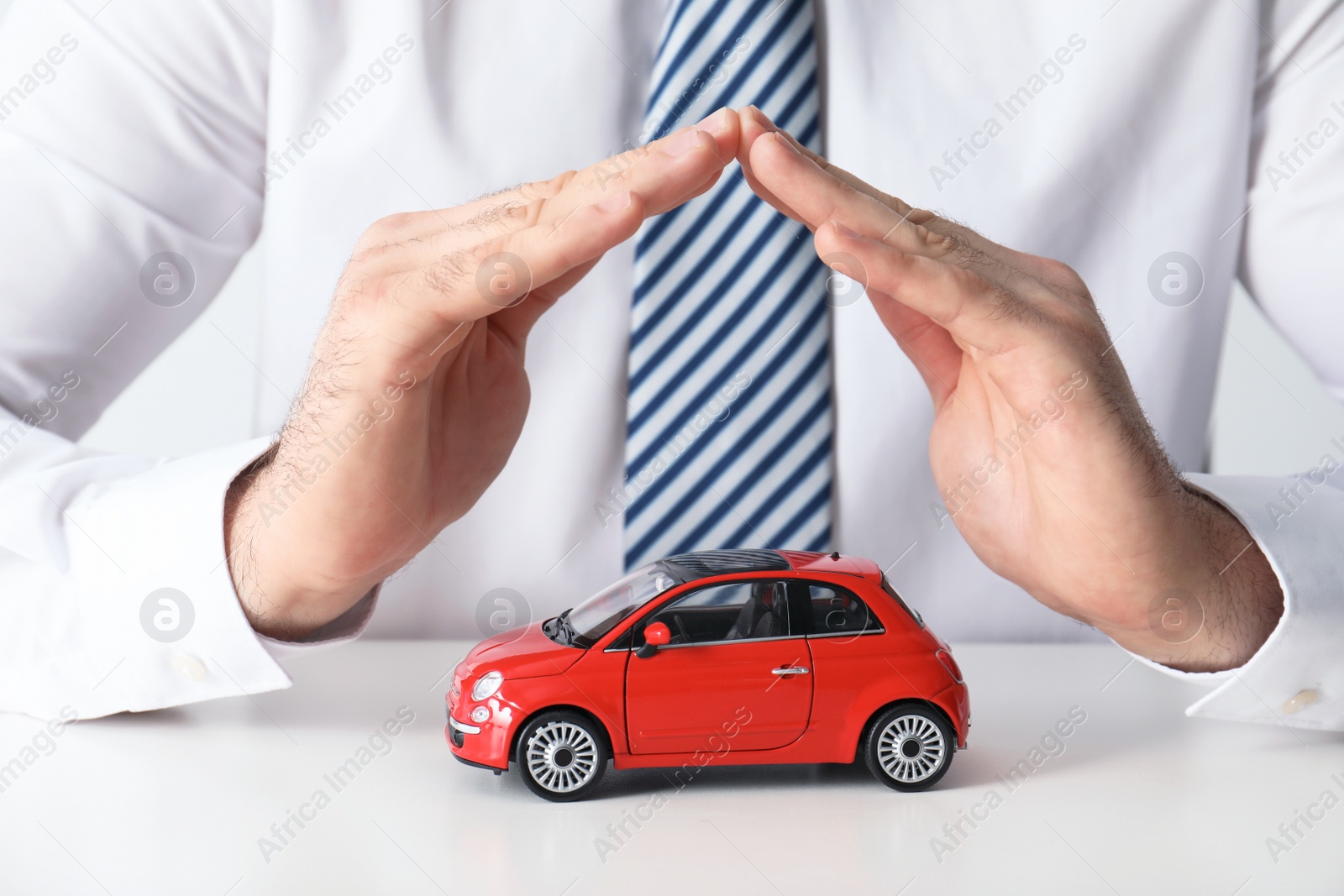 Photo of Male insurance agent covering toy car at table, closeup