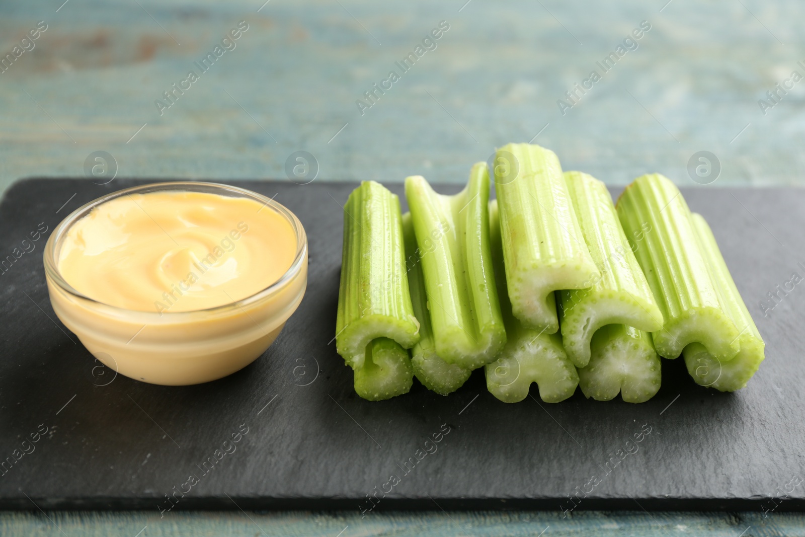 Photo of Celery sticks with dip sauce on slate plate, closeup