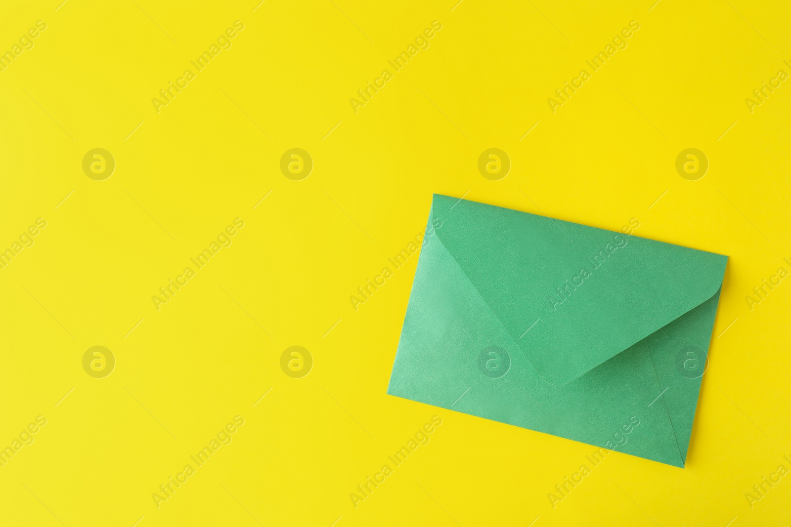 Photo of Green paper envelope on yellow background, top view. Space for text