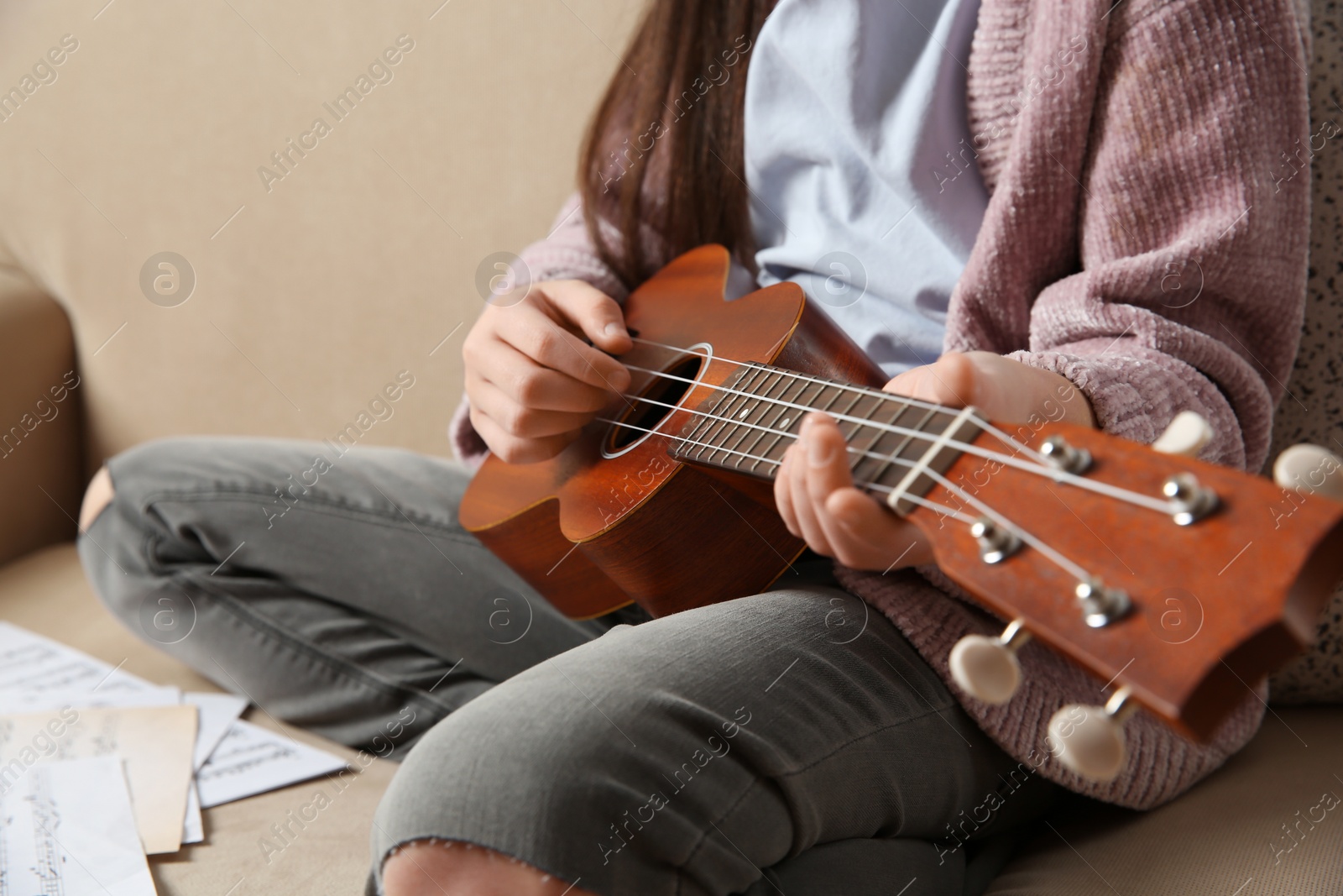 Photo of Little girl playing guitar on sofa, closeup