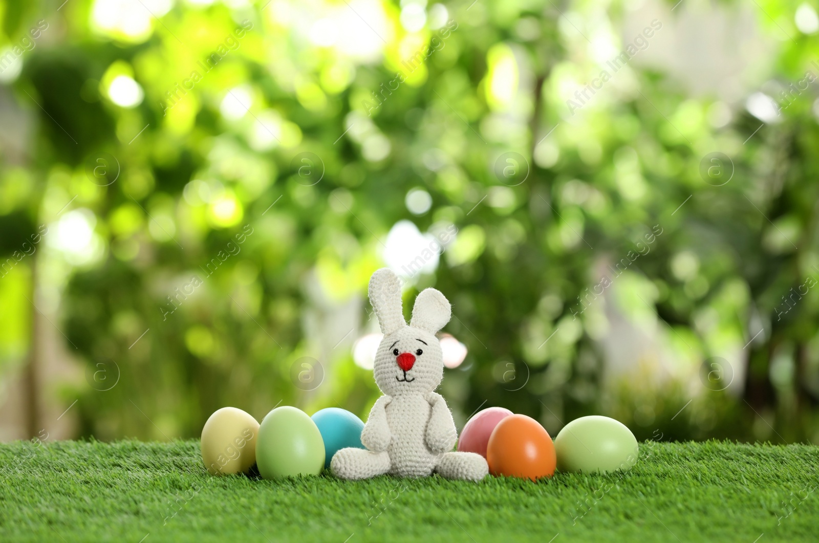 Photo of Cute Easter bunny toy and dyed eggs on green grass against blurred background