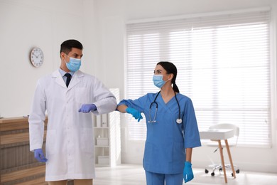 Photo of Doctors with protective masks greeting each other by bumping elbows instead of handshake in clinic