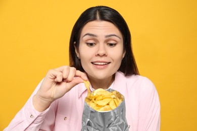 Beautiful woman eating potato chips on orange background