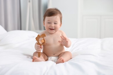 Happy baby boy with wooden rattle on bed at home