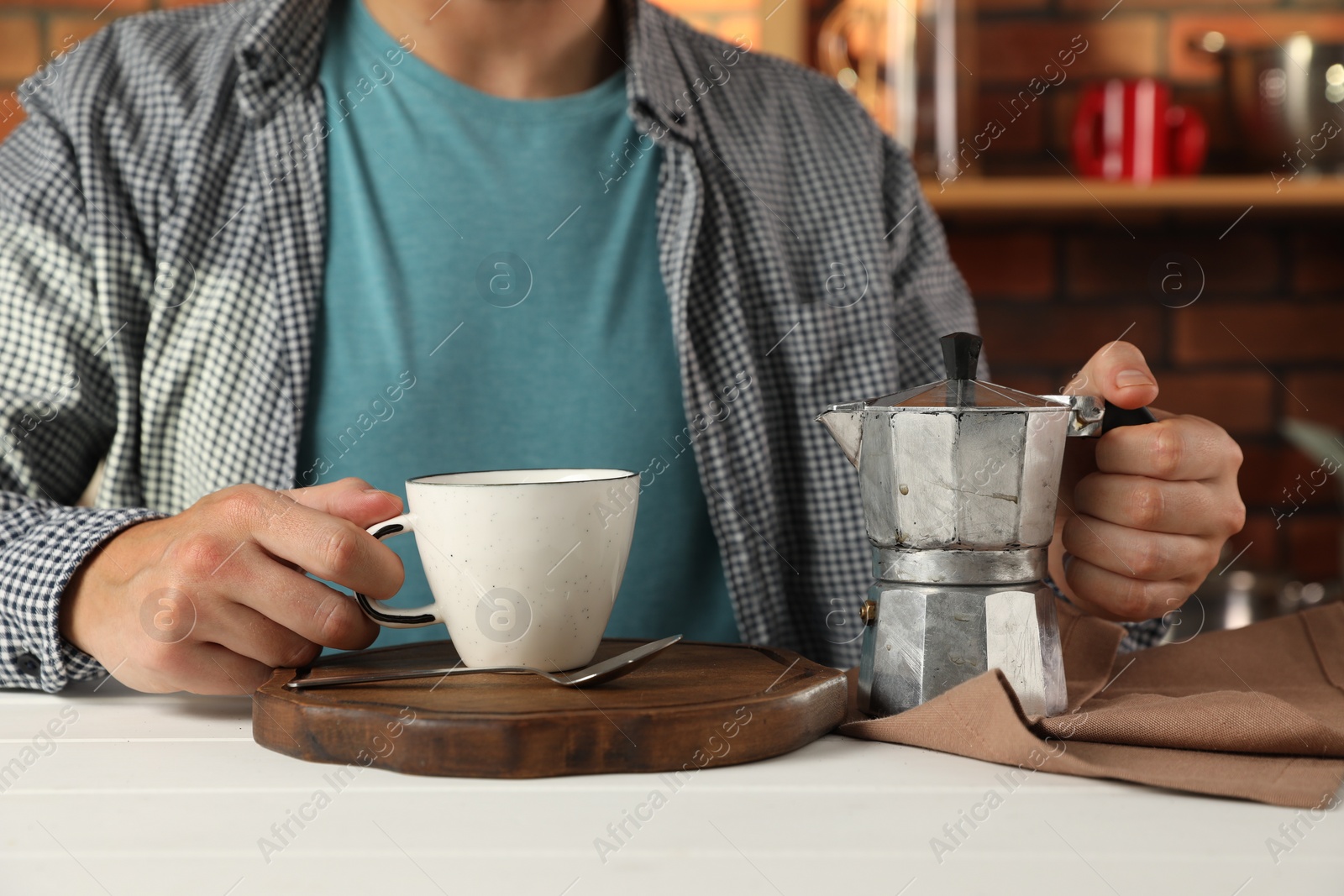 Photo of Brewing coffee. Man with moka pot and cup at white wooden table indoors, closeup