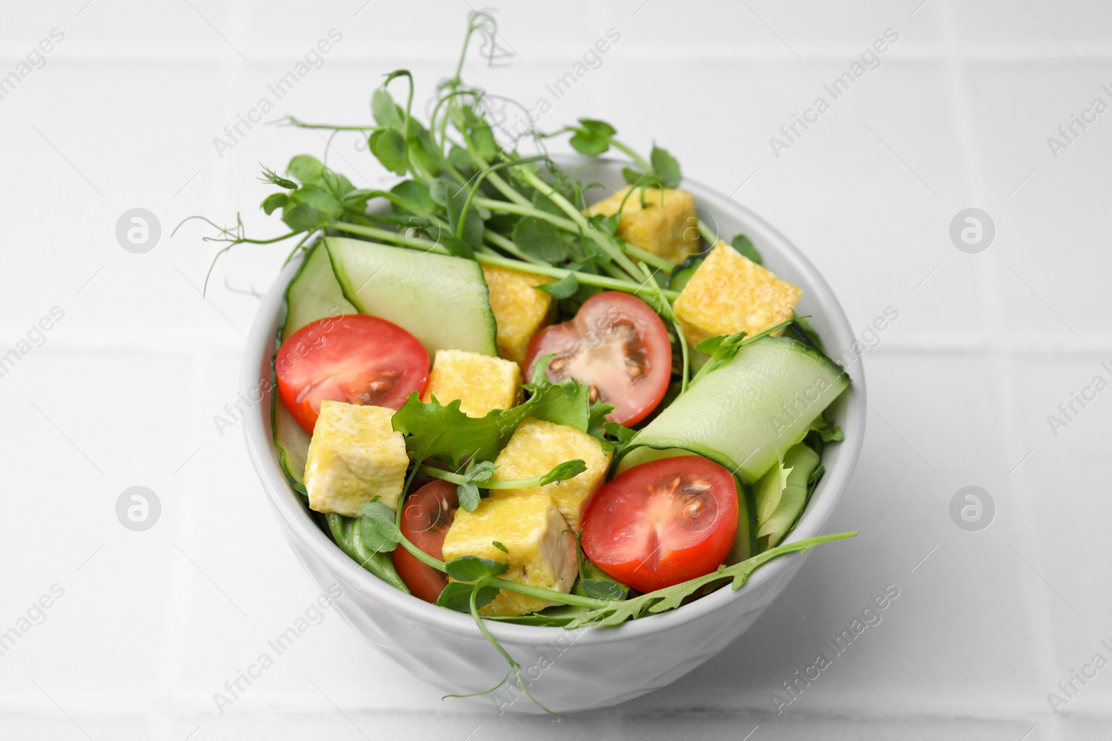 Photo of Bowl of tasty salad with tofu and vegetables on white tiled table