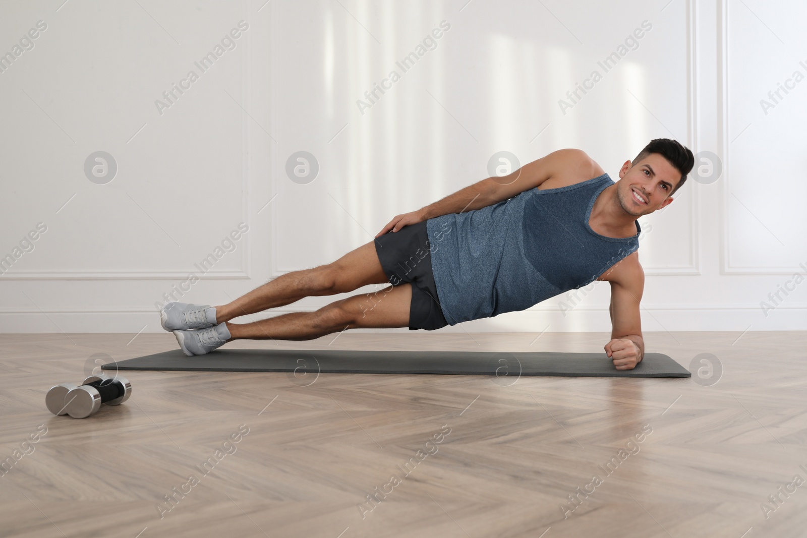 Photo of Handsome man doing side plank exercise on yoga mat indoors