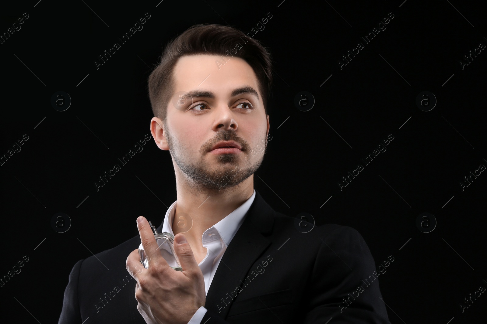 Photo of Handsome man in suit using perfume on black background