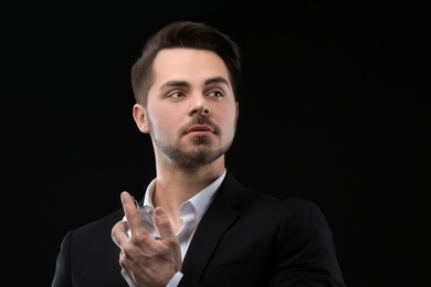 Photo of Handsome man in suit using perfume on black background