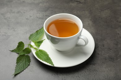 Photo of Cup of aromatic nettle tea and green leaves on grey table