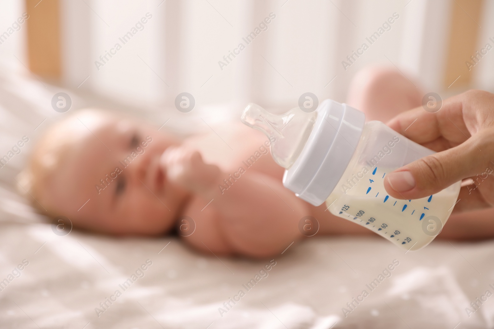 Photo of Healthy baby lying in cot, focus on mother holding milk. Space for text