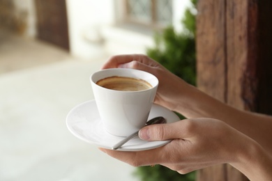 Young woman with cup of delicious coffee on blurred background