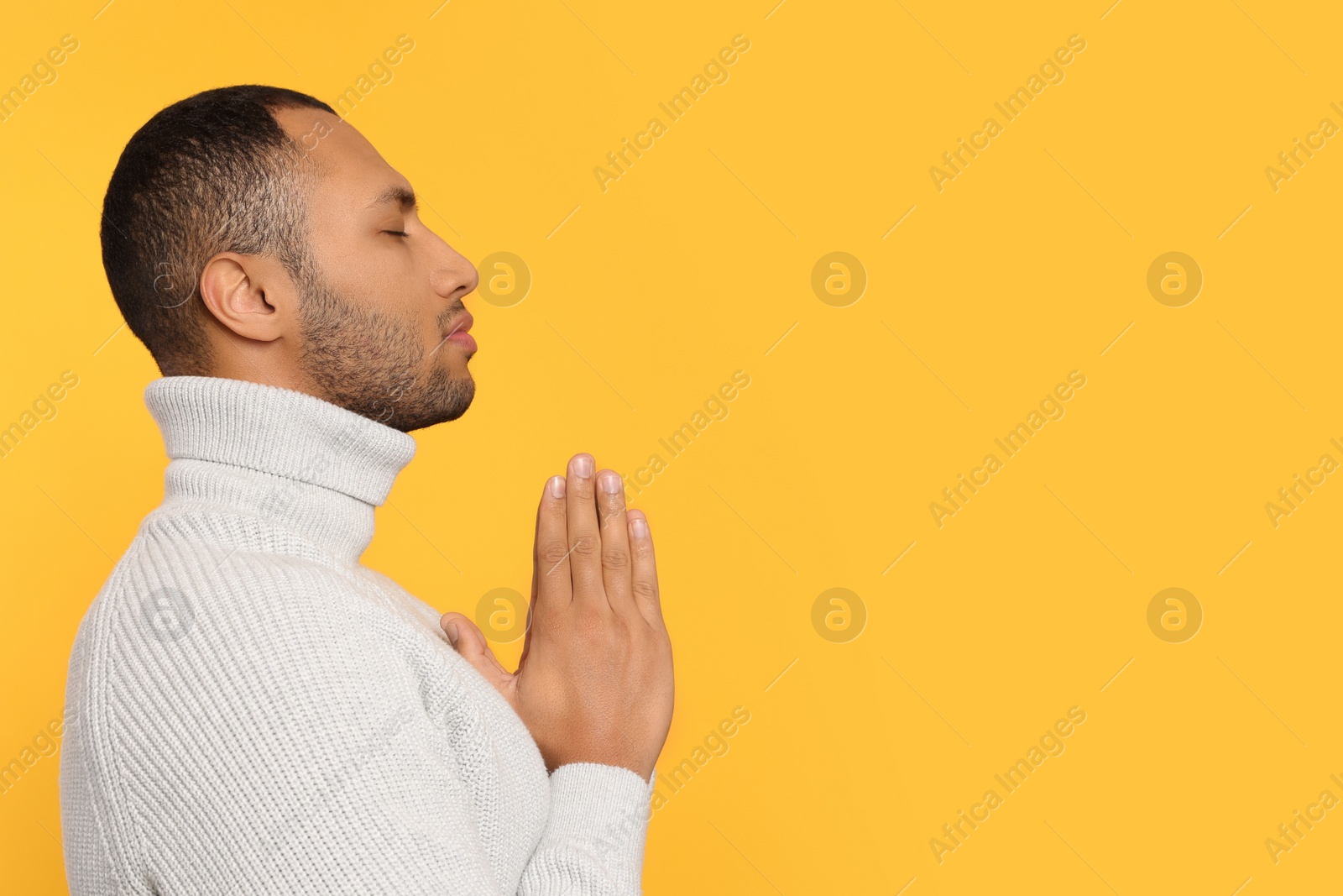 Photo of African American man with clasped hands praying to God on orange background. Space for text