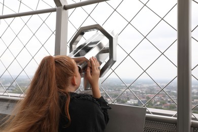 Photo of Teenage girl looking through tower viewer at city, back view. Space for text